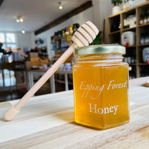 Wooden honey drizzler leaning against a jar of Epping Forest Honey inside Refill Mill shop, Ongar