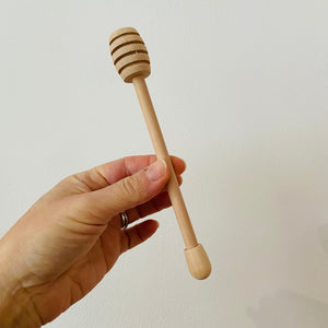 hand holding wooden honey drizzler against a white background