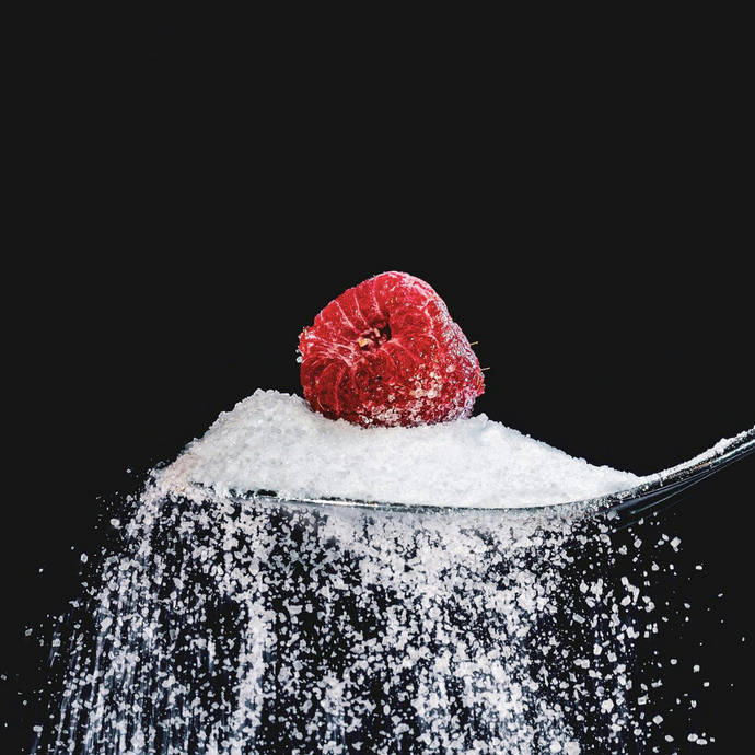 Caster sugar on a spoon and falling down the sides with a raspberry on top, on a black background.