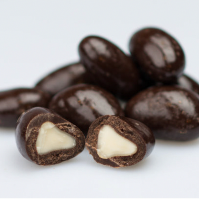 Darl chocolate Brazil nuts piled on table, two cut in half to reveal nut inside.