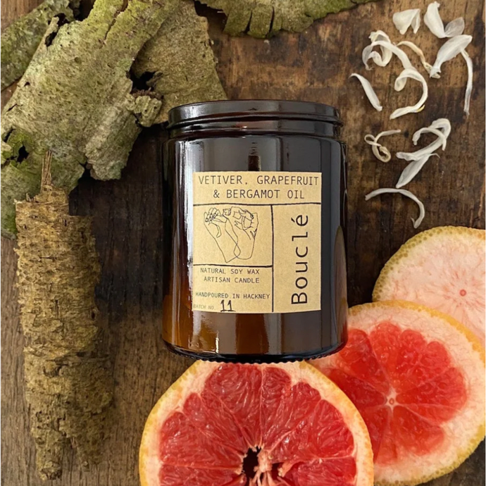 Natural wax candle scented with vetiver, grapefruit and bergamot oil essential oils on a wood background surrounded by grapefruit slices.