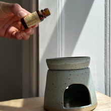 Load image into Gallery viewer, A hand holding a bottle of essential oil aromatherapy scent blend over an oil burner. Refill Mill.
