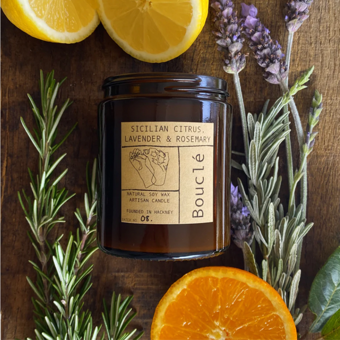 Essential oil blend soy wax candle with lavender, citrus fruits and rosemary surrounding on a wooden background