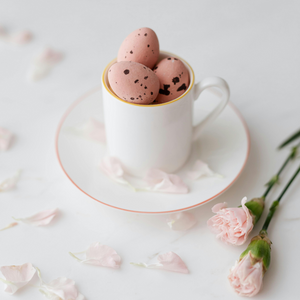 Pink mini eggs in a mini teacup, surrounded by small pink roses and petals