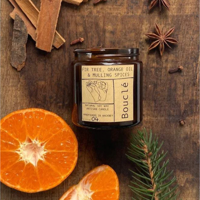 Winter Essential Oil Scented Candle on wooden table with orange slice, fir needles and bark and star anise mulling spices surrounding