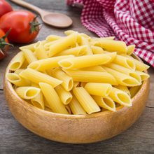 Load image into Gallery viewer, Organic penne pasta in wooden bowl on table with tomatoes, wooden spoon and red cheque napkin in background.
