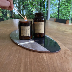 Amber glass jar of safety matches on table next to aromatherapy essential oil scent blended artisan candle being lit with one of the matches.