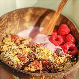 Handmade granola with toasted pecans, yoghurts and fresh raspberries inside a coconut bowl with wooden spoon