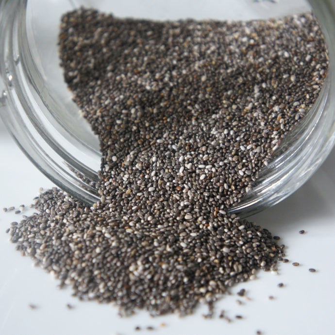 Chia Seeds spilling out of glass jar onto white surface.